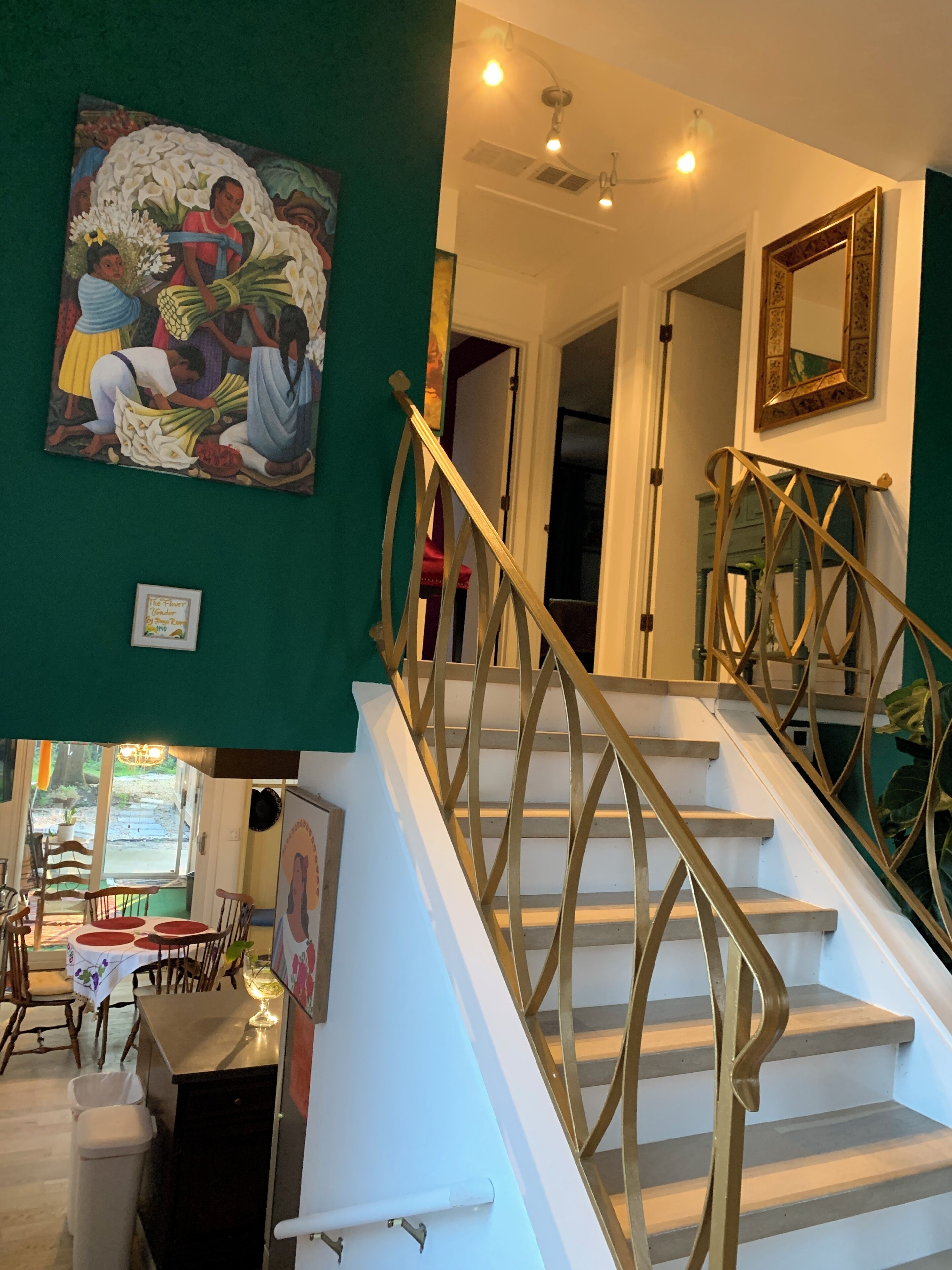 Un escalier avec une rampe dorée menant à une pièce dont le mur est vert et qui contient un tableau.