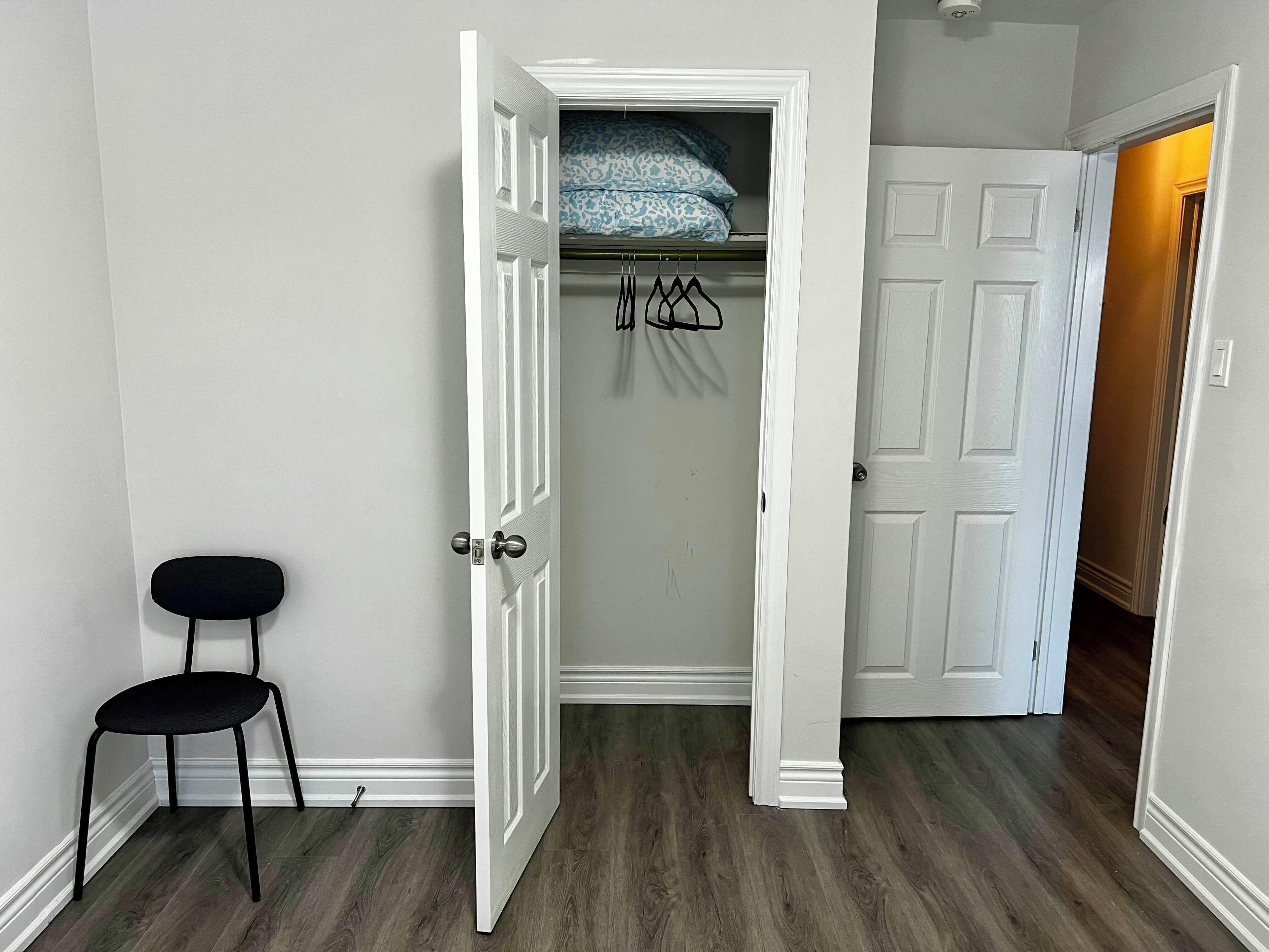A hallway with a white door leading to a closet with hanging clothes.