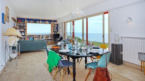 A dining area with a view of the sea, a bookshelf, and a cozy seating area.