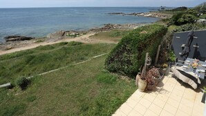 A terrace with a view of the sea, a dining area with outdoor furniture, and a garden with potted plants.