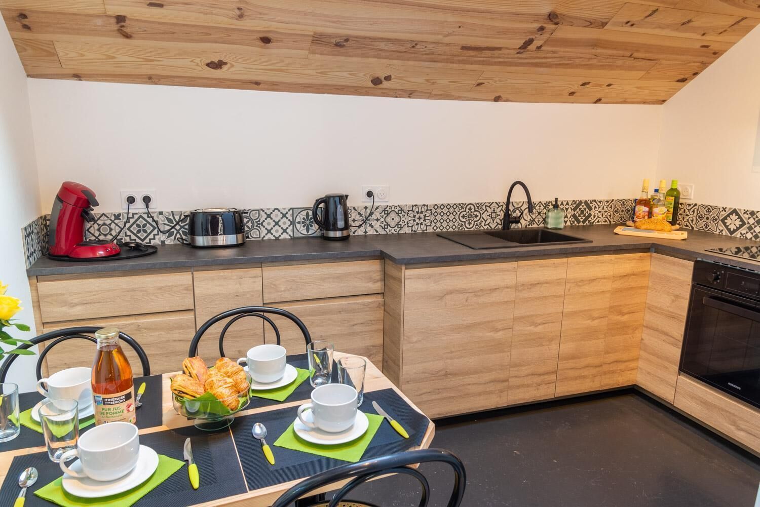 Eine moderne Küche mit Holzschnitzarbeiten, einer schwarzen Arbeitsplatte und einem Essbereich mit Tisch für zwei Personen.