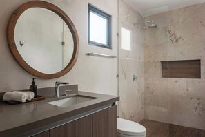 Une salle de bain moderne avec un grand miroir rond, un lavabo, des toilettes et une douche.