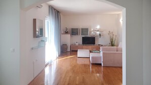 Ein modernes Wohnzimmer mit Holzboden, einer Couch, einem Fernseher und einem Essbereich.