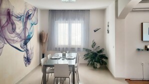Ein moderner Essbereich mit einem Glastisch, weißen Stühlen und einem großen abstrakten Gemälde an der Wand.
