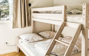 Una cama litera con ropa de cama y almohadas blancas, una escalera de madera y una ventana con cortinas.