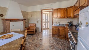 Una cocina con armarios de madera, una mesa de comedor con un mantel individual, un sofá y vistas al exterior a través de una puerta.