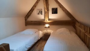 Une petite chambre accueillante avec deux lits simples, des poutres en bois au plafond et une table de chevet avec une lampe.
