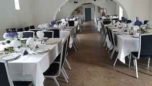 Une grande salle à manger avec des tables et des chaises blanches, décorée de fleurs bleues et de nappes blanches.