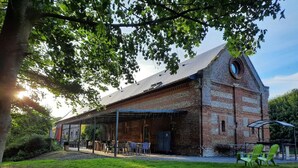 Un bâtiment rustique en briques, doté d’un patio couvert, d’un espace extérieur aménagé avec des sièges et d’une pelouse verdoyante.