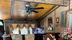 Un salón acogedor con techo de madera, un ventilador de techo, un televisor, un sofá, una mesa de comedor y una alfombra estampada.