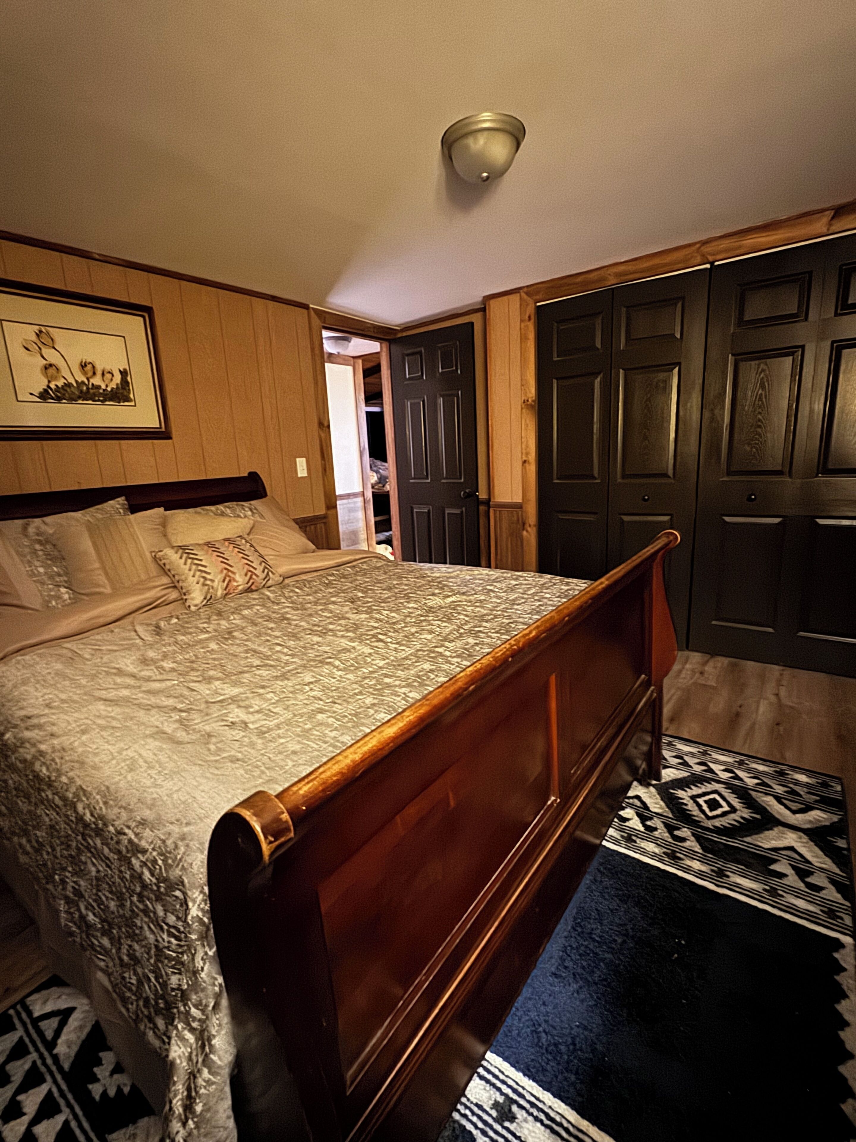 Une chambre à coucher avec un lit en bois, une porte sombre et un tableau encadré accroché au mur.
