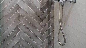 Una ducha con manguera de cromo y cabezal de ducha de mano frente a un pared de azulejos tipo espiga.