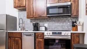 Una cocina con armarios de madera, un refrigerador de acero inoxidable, una cafetera, un microondas, un lavavajillas y un horno.