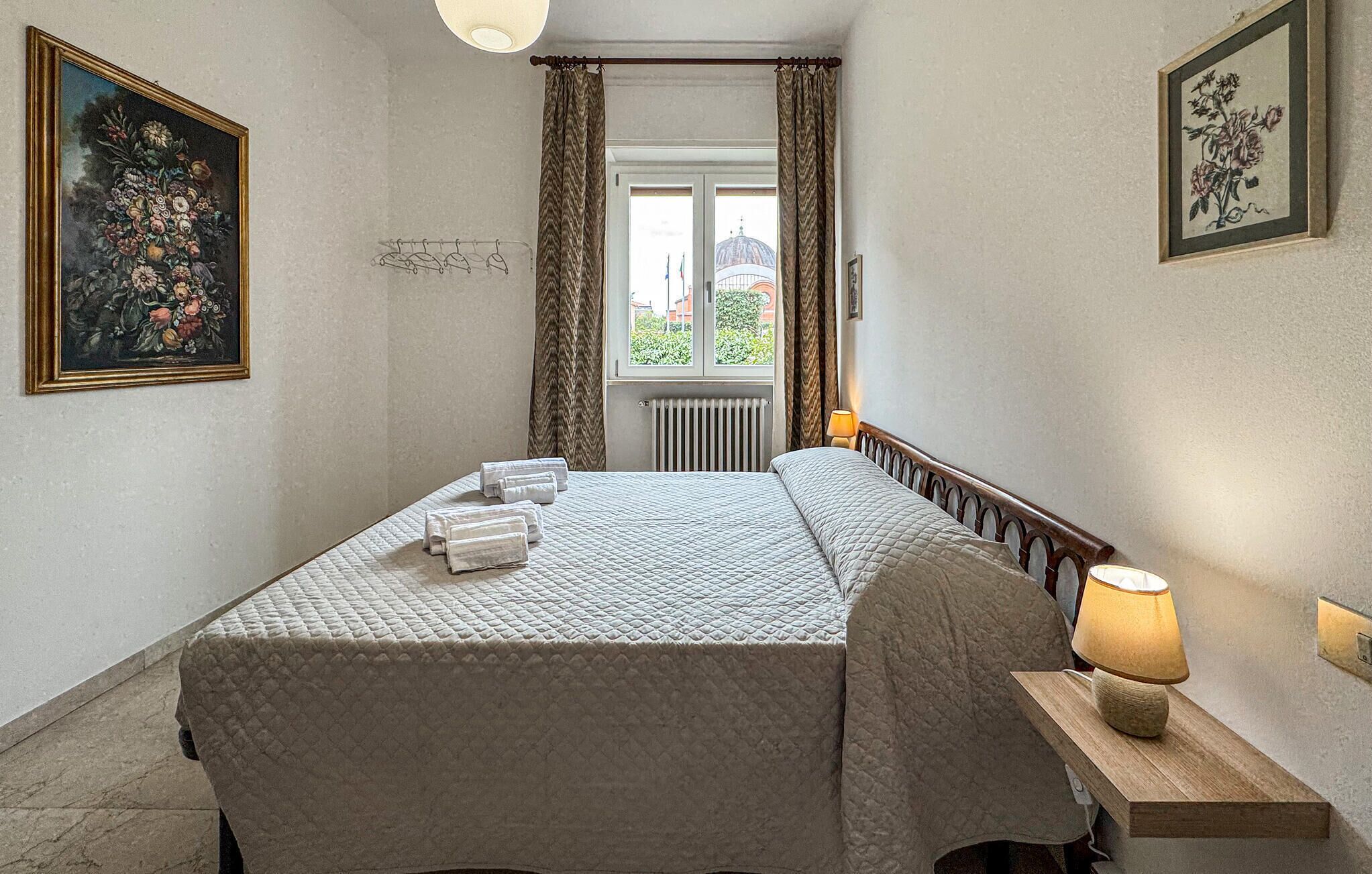 Un lit bien fait, recouvert d’une courtepointe, une lampe de chevet et une fenêtre avec des rideaux.