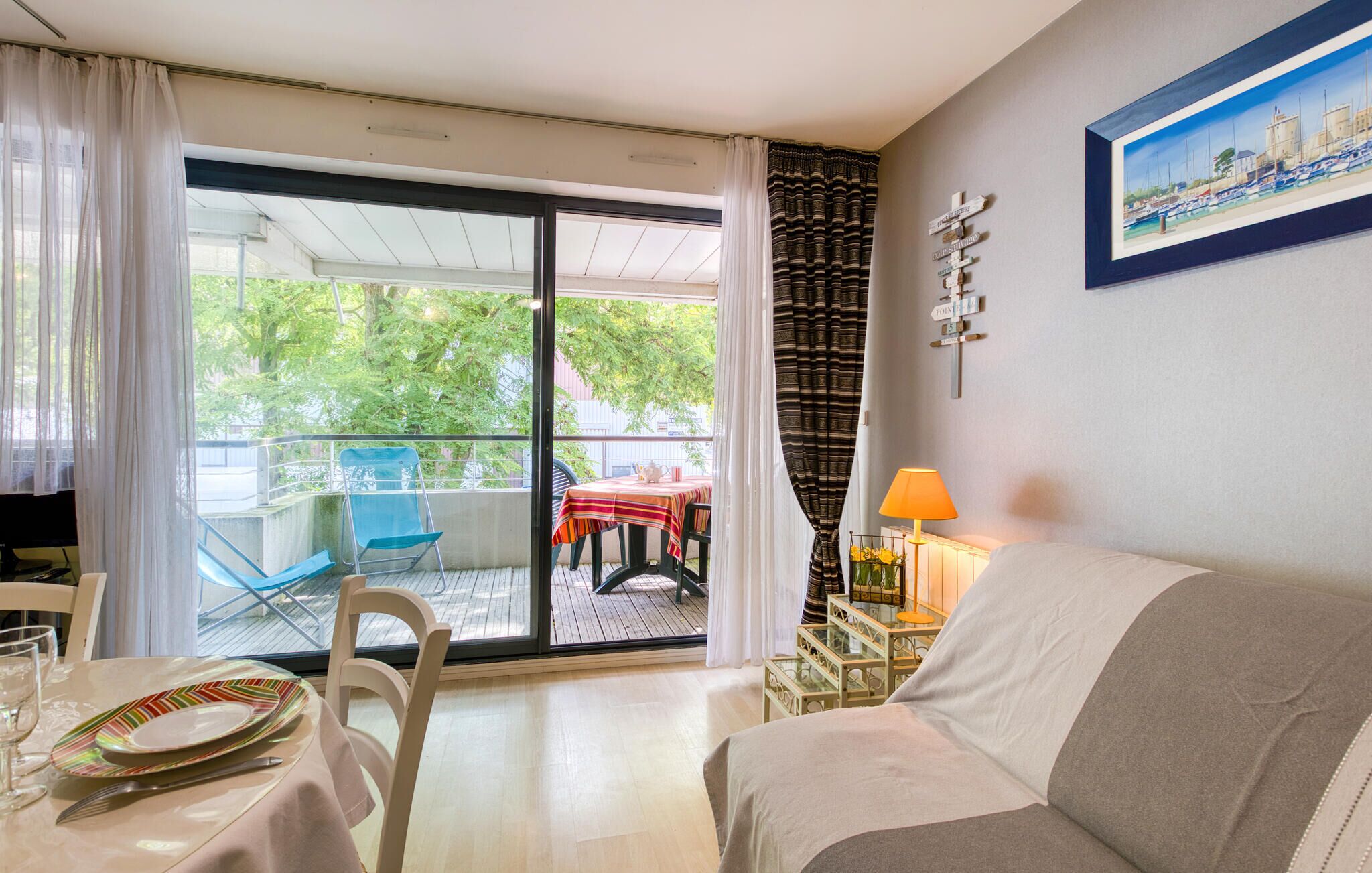 Habitación de hotel con balcón, una mesa de comedor con sillas, un sofá, un televisor y una lámpara.