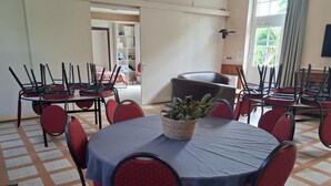 A conference room with round tables, red chairs, and a potted plant.