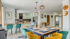 A modern kitchen with white cabinets, a central island, and a dining area with a wooden table and colorful chairs.