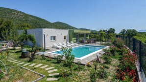 A modern house with a swimming pool, surrounded by a garden and a mountain backdrop.