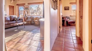 A spacious living area with a wooden ceiling, a fireplace, and a large window providing natural light.
