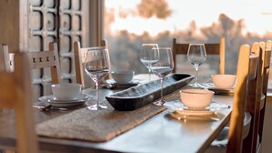 A dining table set with wine glasses, bowls, and cutlery, with a view of trees through a window.