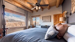 A bedroom with a large bed, a ceiling fan, a view of mountains, and a wooden ceiling.