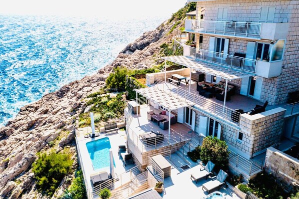 A multi-story building with a pool, outdoor seating, and a view of the sea.