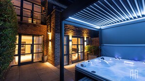 A modern outdoor hot tub area with a brick building, glass doors, and a wooden deck. - AYLI (London)