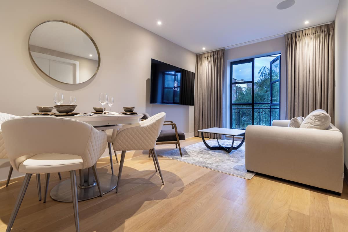 A modern living room with a dining area, a sofa, a TV, and a large window with curtains.