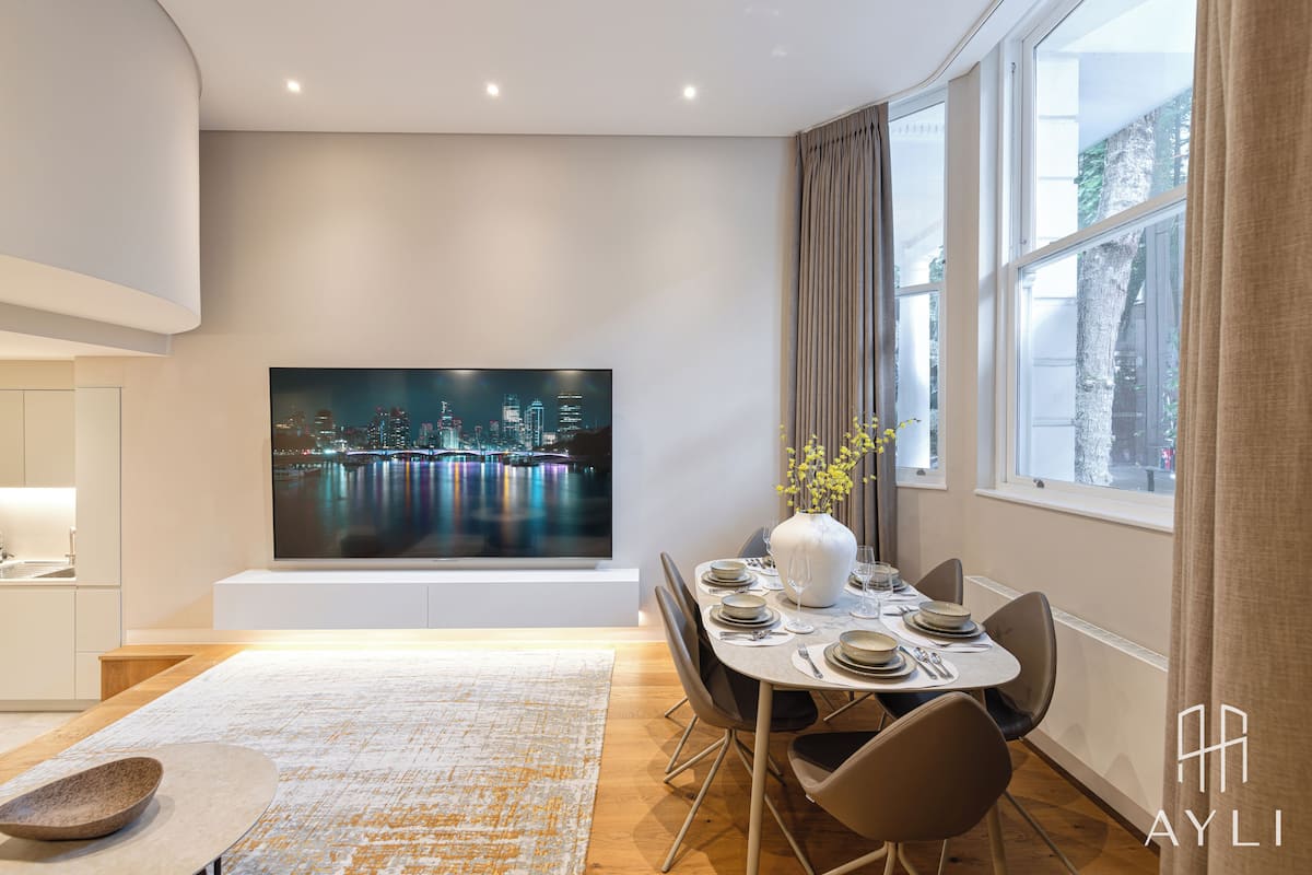 A modern dining area with a cityscape painting, a vase with flowers, and a large window with curtains.