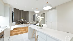 A modern kitchen with white cabinetry, a wooden countertop, and a dining area with a table and chairs. - AYLI (London)