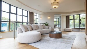 A spacious living room with a large sectional sofa, a round coffee table, and a view of the outdoors through large windows. - AYLI (London)