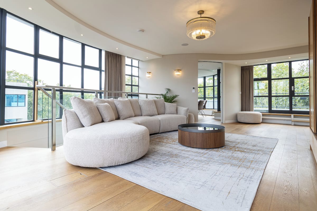 A spacious living room with a large sectional sofa, a round coffee table, and a view of the outdoors through large windows.