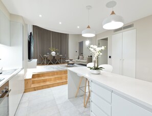 A modern kitchen with white cabinetry, a wooden countertop, and a dining area with a table and chairs. - AYLI (London)