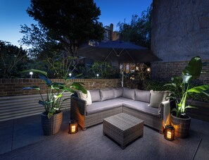A modern outdoor seating area with a sectional sofa, a coffee table, and potted plants. - AYLI (London)