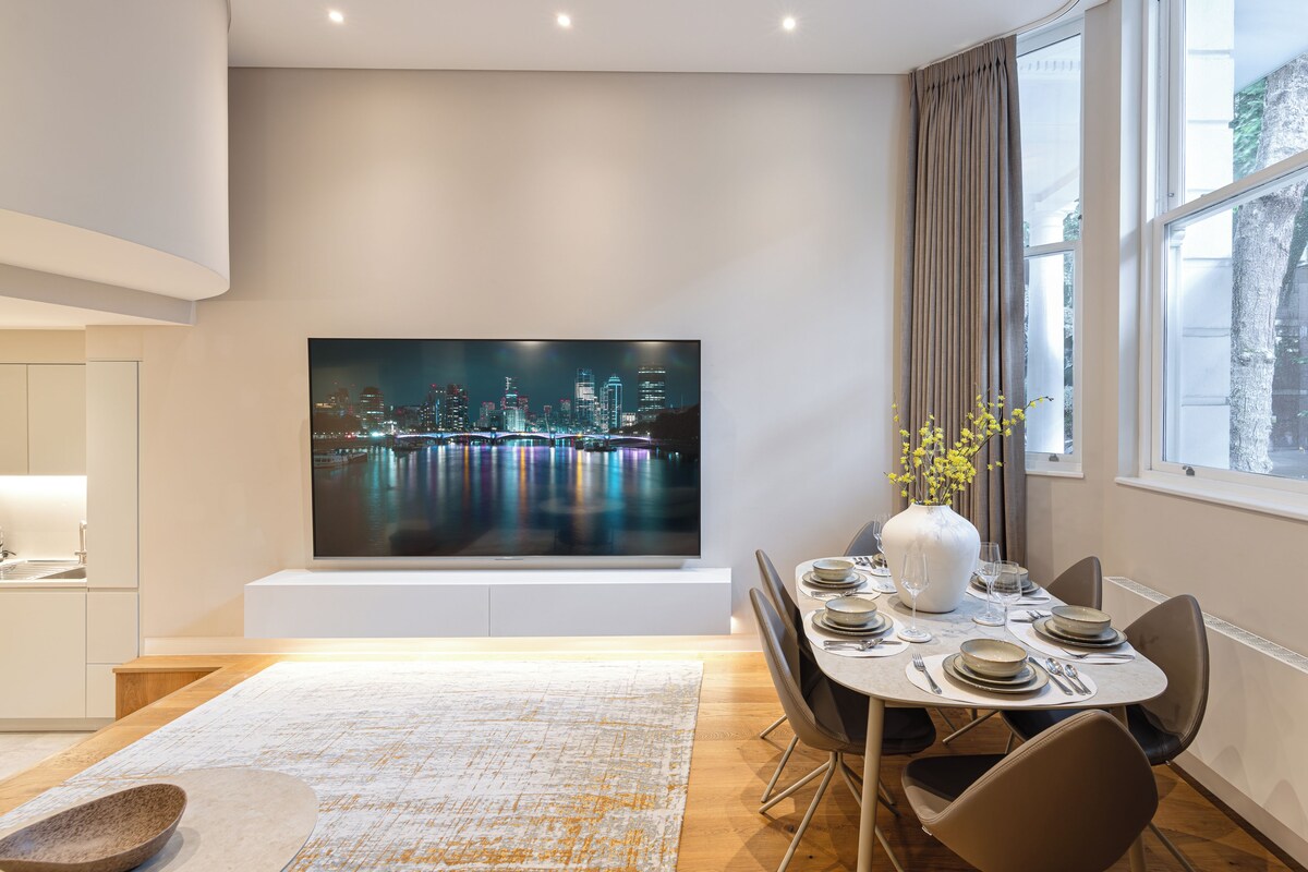 A modern dining area with a cityscape painting, a vase with flowers, and a large window with curtains.