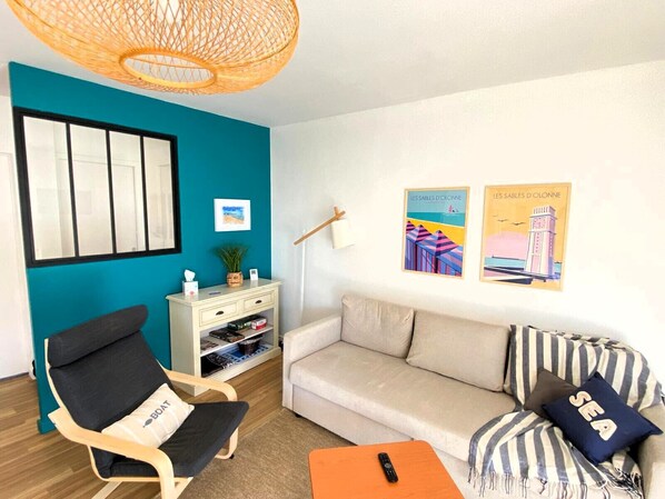 Una sala de estar con una pared de acento color turquesa, un sofá, un sillón, una mesita y una lámpara colgante.