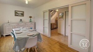 A dining area with a table set for four, a white cabinet with drawers, and a staircase leading to another room. - Les Pâquerettes - PLENEUF VAL ANDRE (PLENEUF VAL ANDRE)