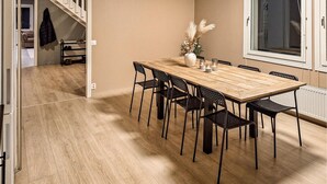 A dining area with a wooden table and black chairs, a vase with dried flowers, and a window with blinds.