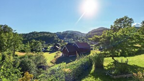 A rural landscape with a house surrounded by greenery and hills.
