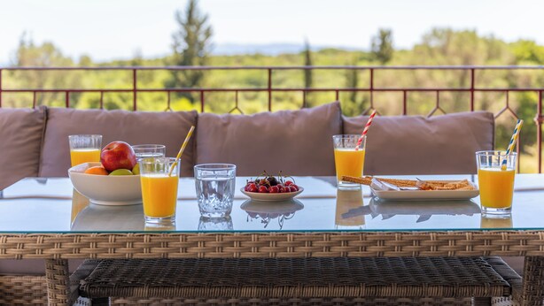 Une table de petit-déjeuner avec des fruits, du jus et des céréales, placée sur un balcon donnant sur un paysage magnifique.