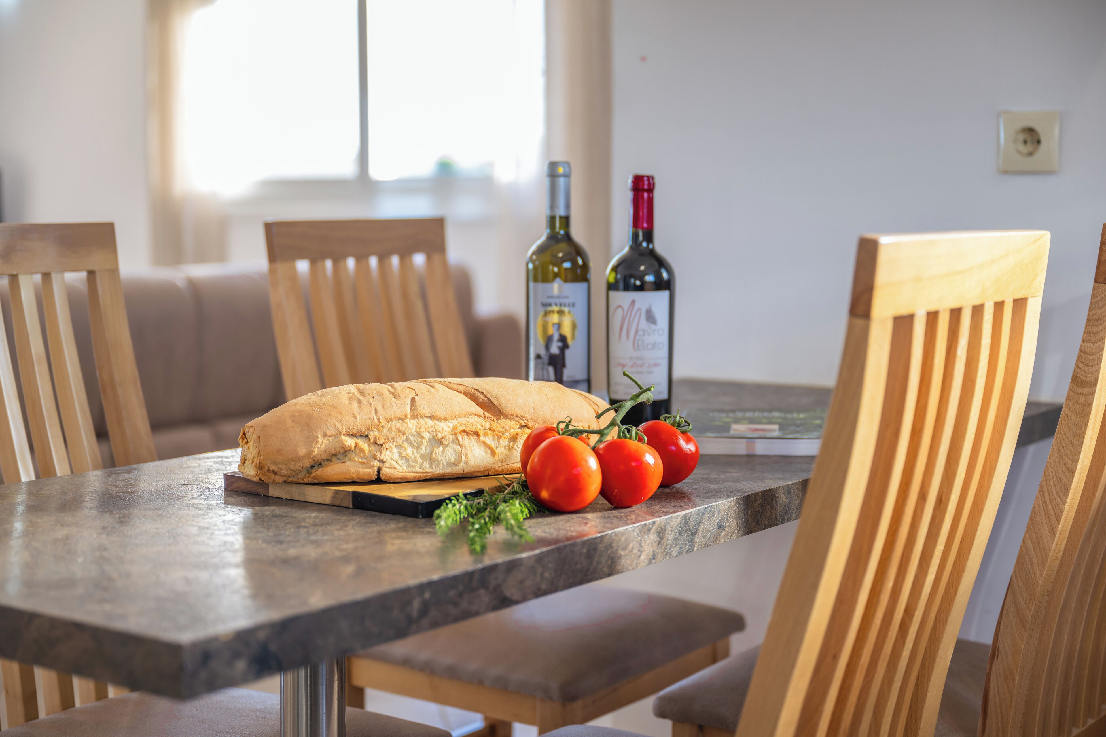 Une table à manger avec une miche de pain, des tomates et des bouteilles de vin.