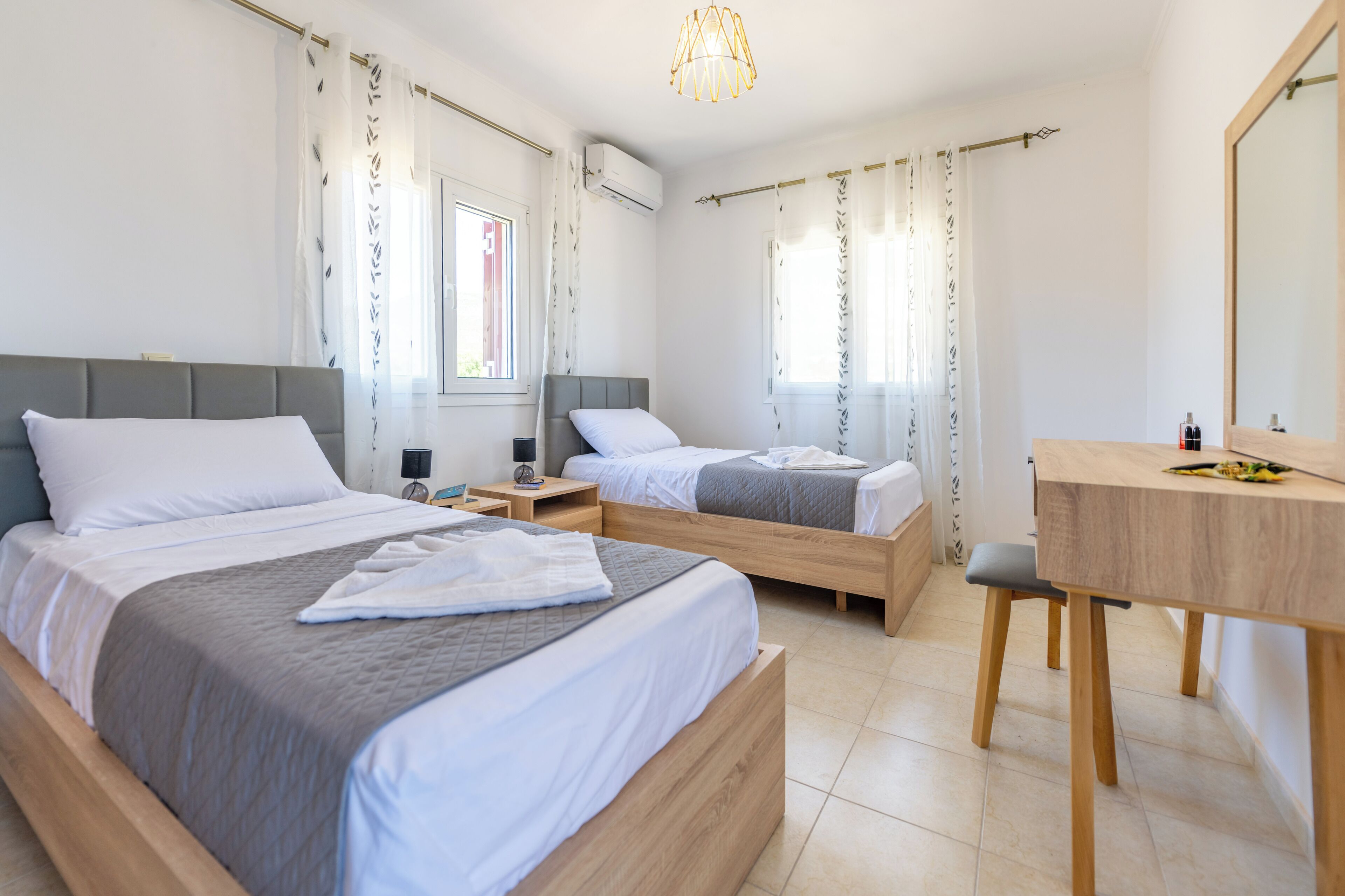 A modern hotel room with two single beds, a wooden desk, a chair, and a large mirror.