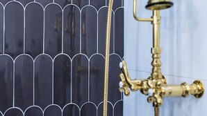 Een badkamer met een zwart-wit betegelde muur, een gouden douchekop en een zichtbare leiding.