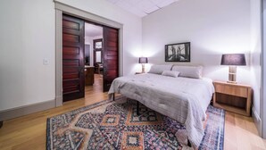 Een slaapkamer met een bed, nachtkastjes, een kroonluchter, een schilderij en een kamerbreed tapijt.