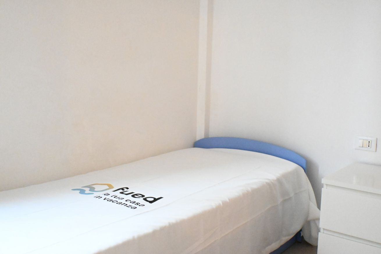 A single-bed room with a white bedspread, a blue headboard, and a white dresser.