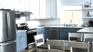 Cozinha moderna com armários brancos, eletrodomésticos de aço inoxidável e uma área de jantar com cadeiras brancas.