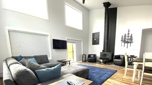 Uma sala de estar moderna com um sofá cinza, almofadas azuis, uma mesa de centro de madeira e um tapete azul. Há uma lareira com uma TV fixada na parede.