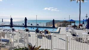 Área da piscina com espreguiçadeiras e guarda-sóis, um deck de madeira e vista para o oceano.