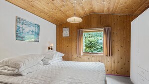 Un dormitorio con techo de madera, una cama con ropa de cama blanca, una ventana con cortinas y una lámpara fijada a la pared.