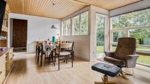 Una habitación acogedora con pisos de madera, una mesa de comedor con sillas, un sofá de cuero y ventanas amplias que dan a vistas de vegetación.